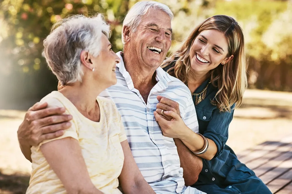 An adult daughter, sitting next to her older adult, senior parents; everyone is happy, smiling, laughing, and healthy.